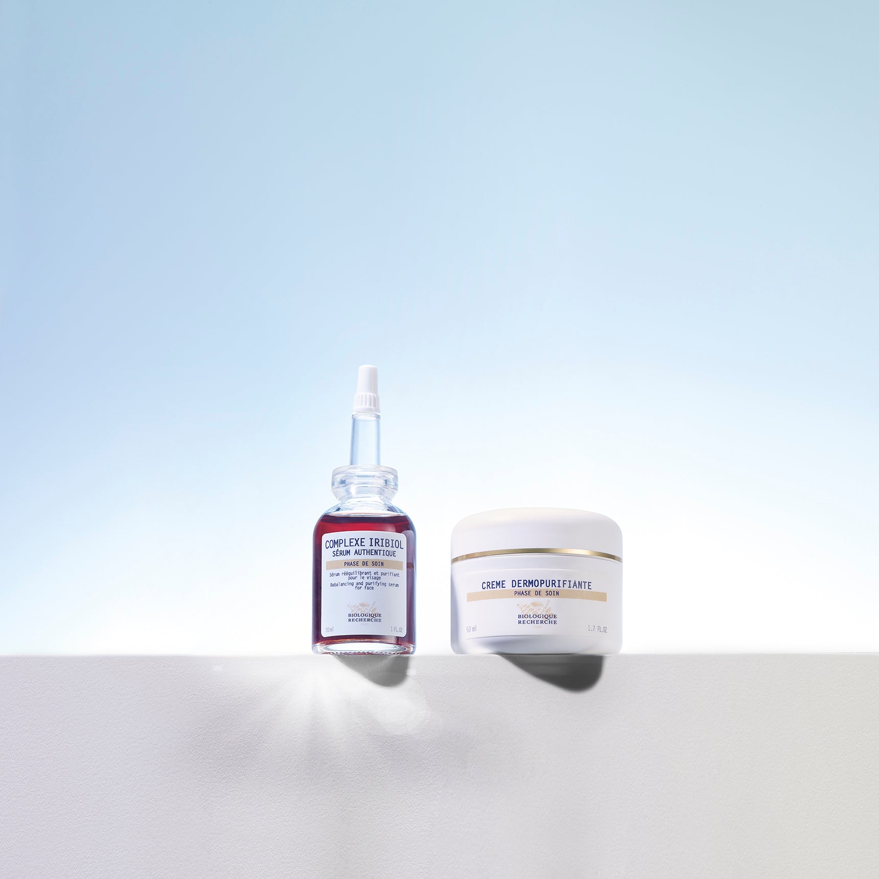 Biologique Recherche Crème Dermopurifiante white jar and dark glass serum bottle with dropper on white surface with blue.