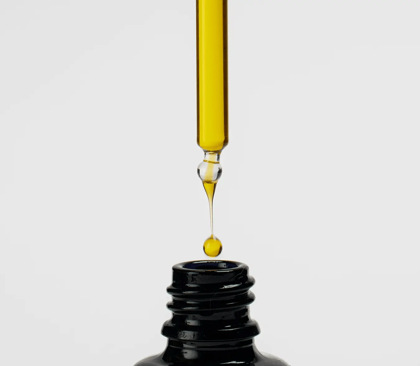 Golden yellow dropper dispensing serum above black glass bottle opening.