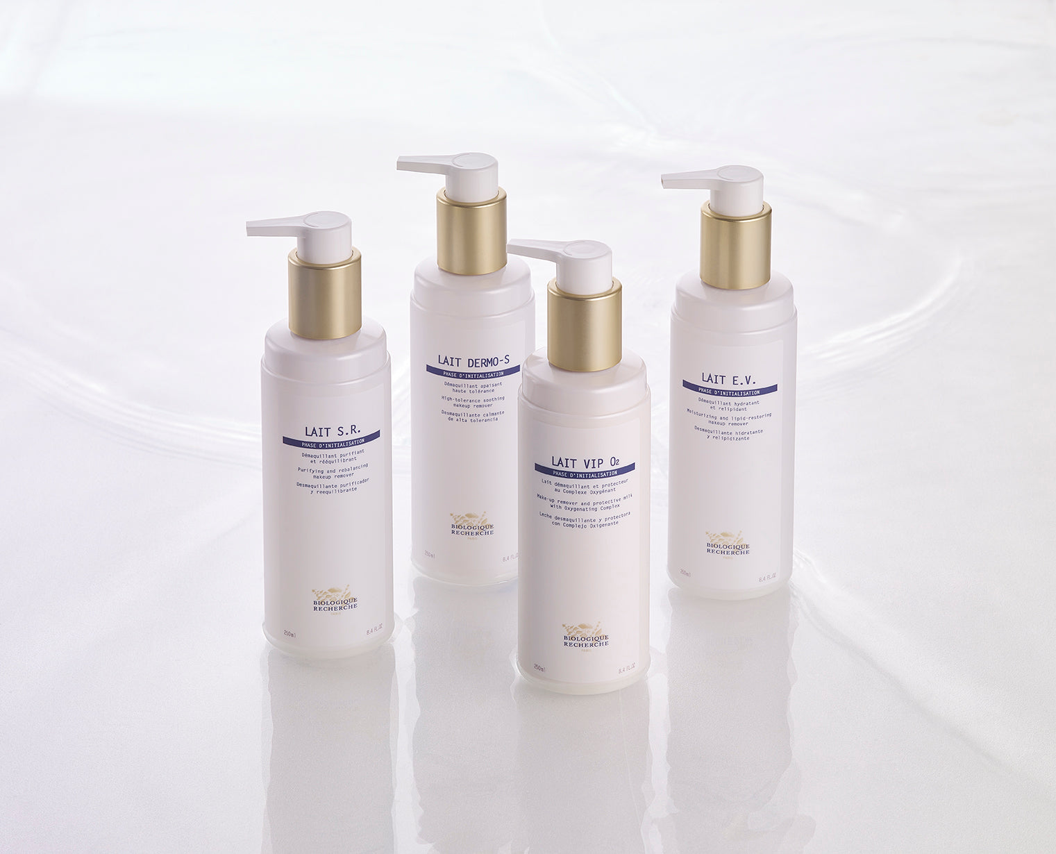 Four frosted white Biologique Recherche Lait VIP O2 bottles with gold pump caps arranged on a glossy white surface.