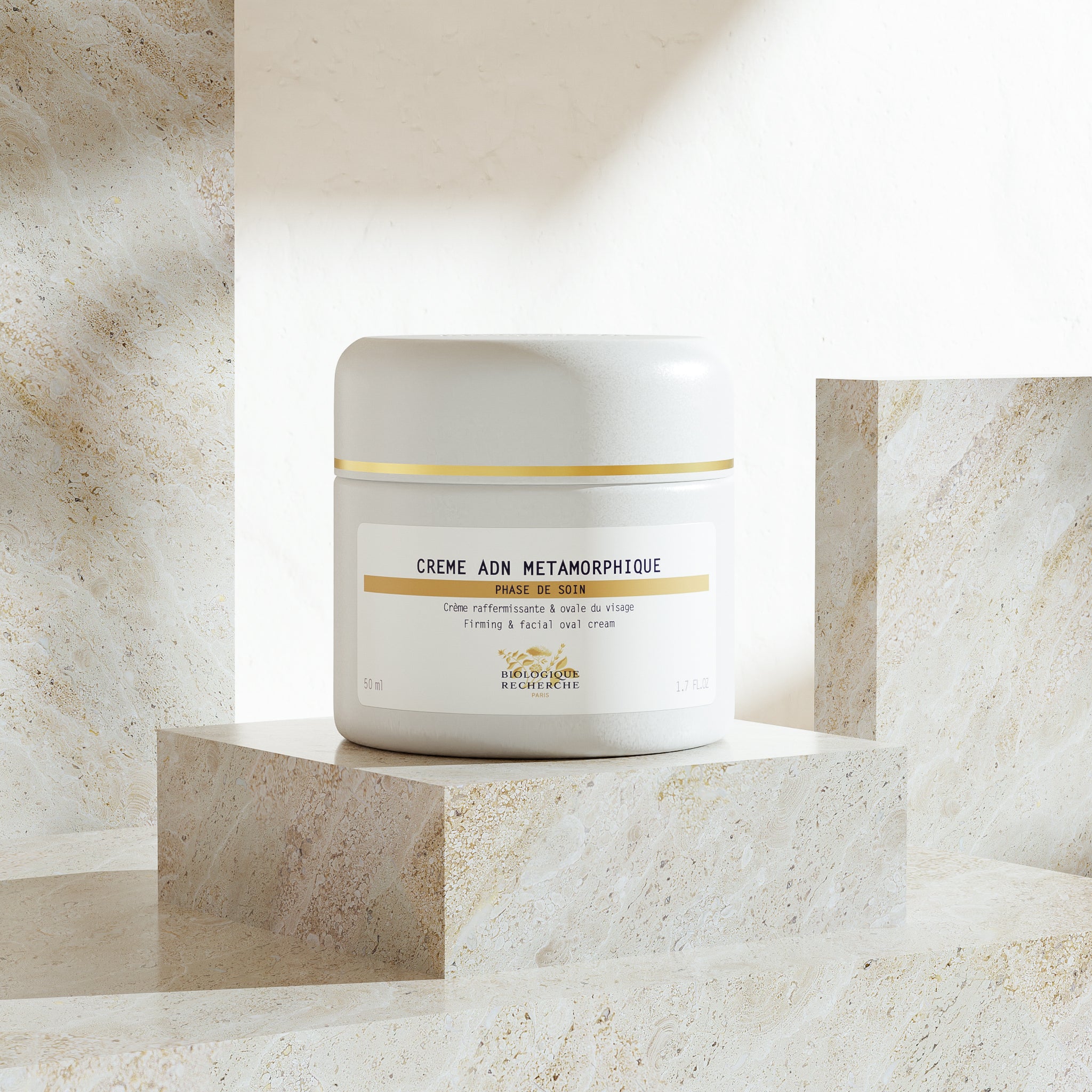 White jar of CRÈME PTO MÉTAMORPHIQUE moisturizer with gold accents on beige marble stepped display.