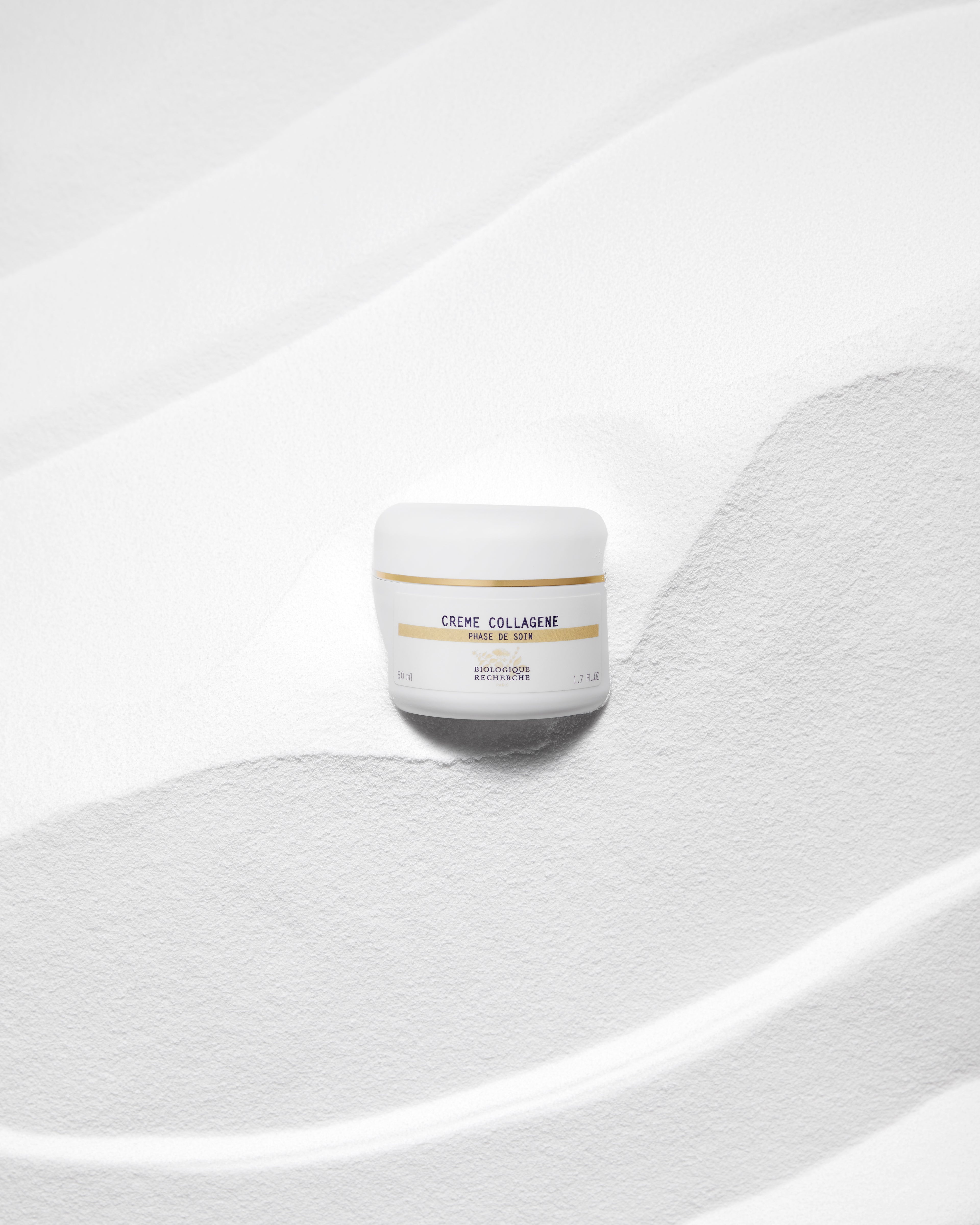 White jar of Crème Collagène moisturizer with gold and black text on textured white background.