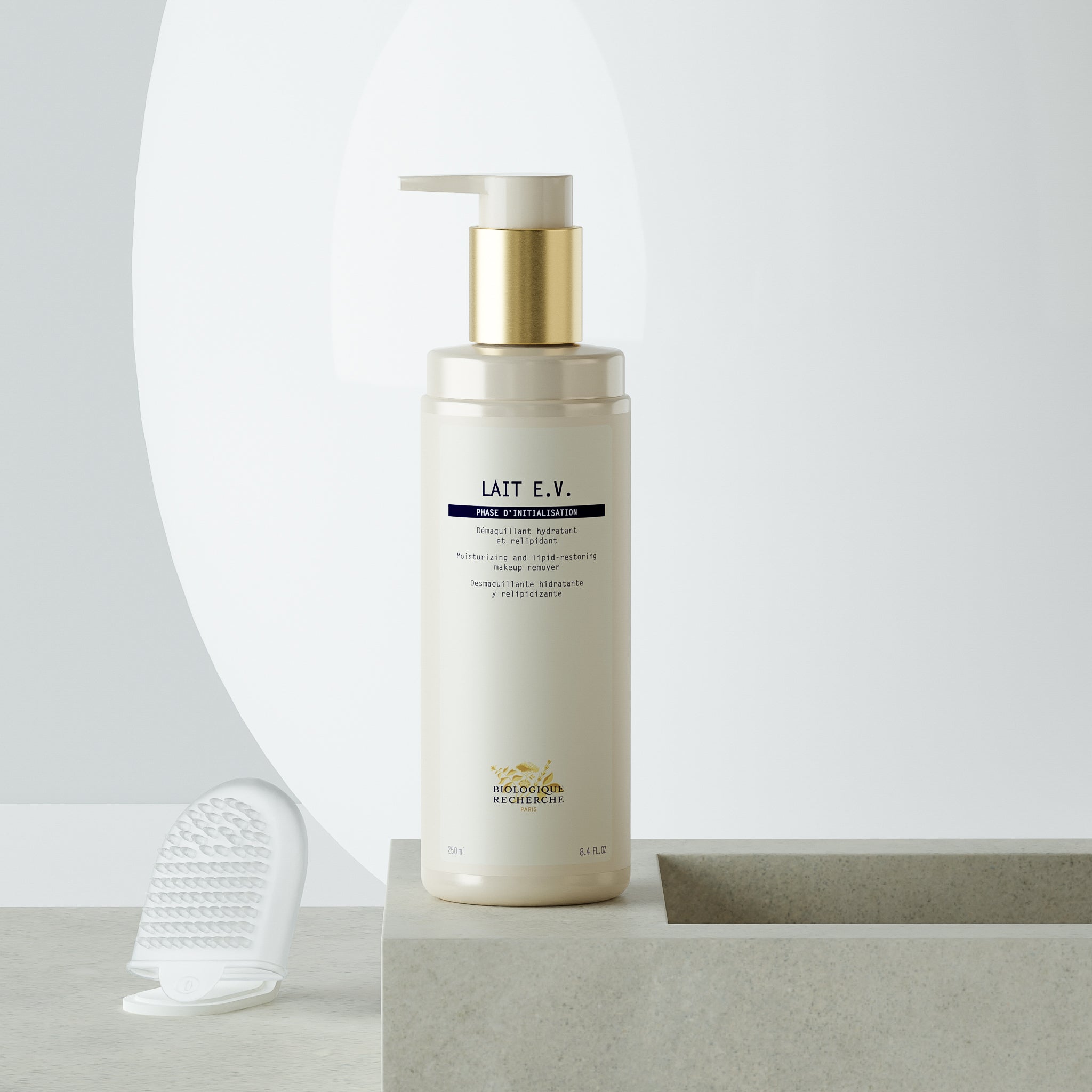White plastic bottle of Lait E.V. milk cleanser with gold pump and blue label text on white surface with clear silicone.