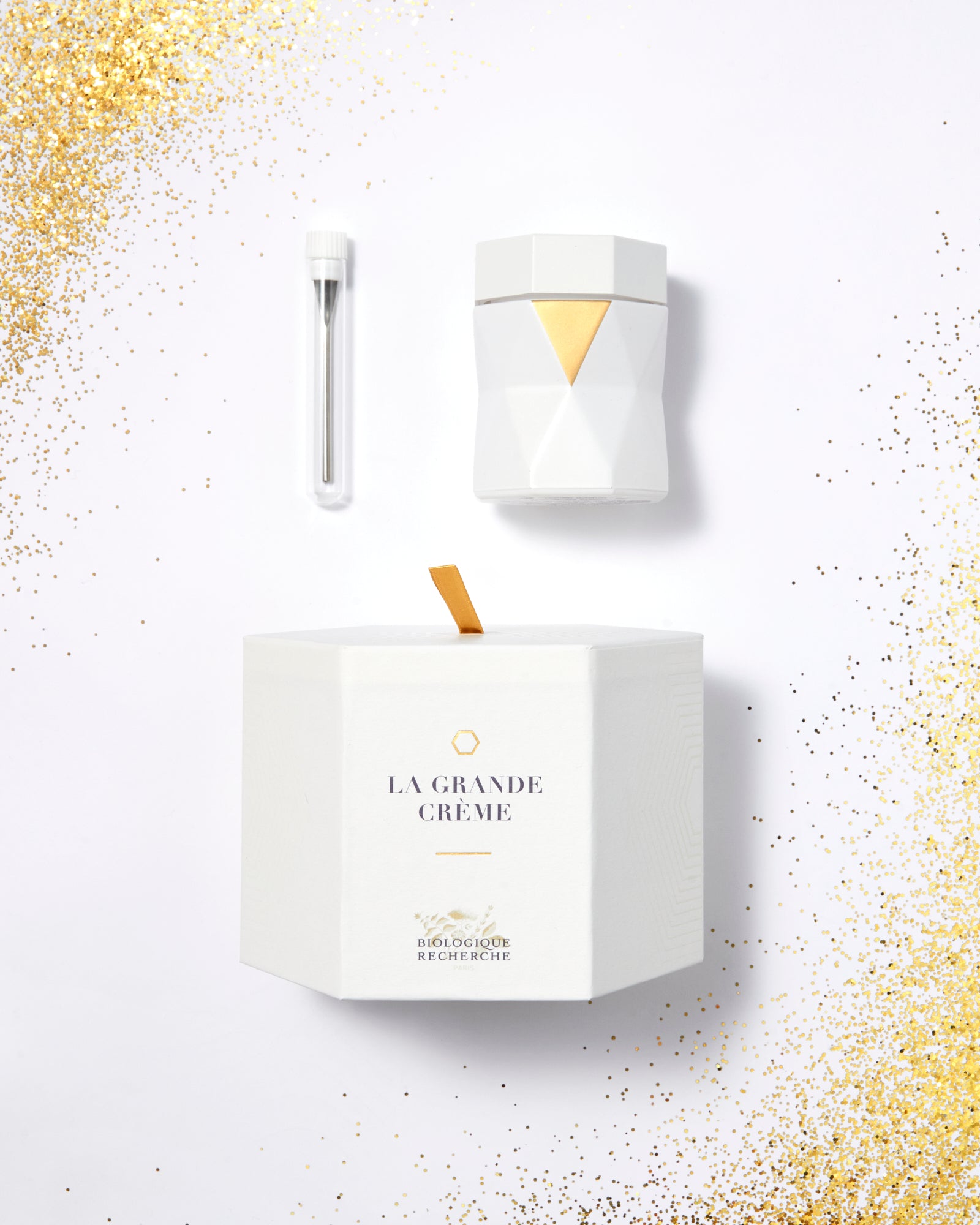 White hexagonal jar of La Grande Crème with gold accents, accompanied by a small white applicator brush.