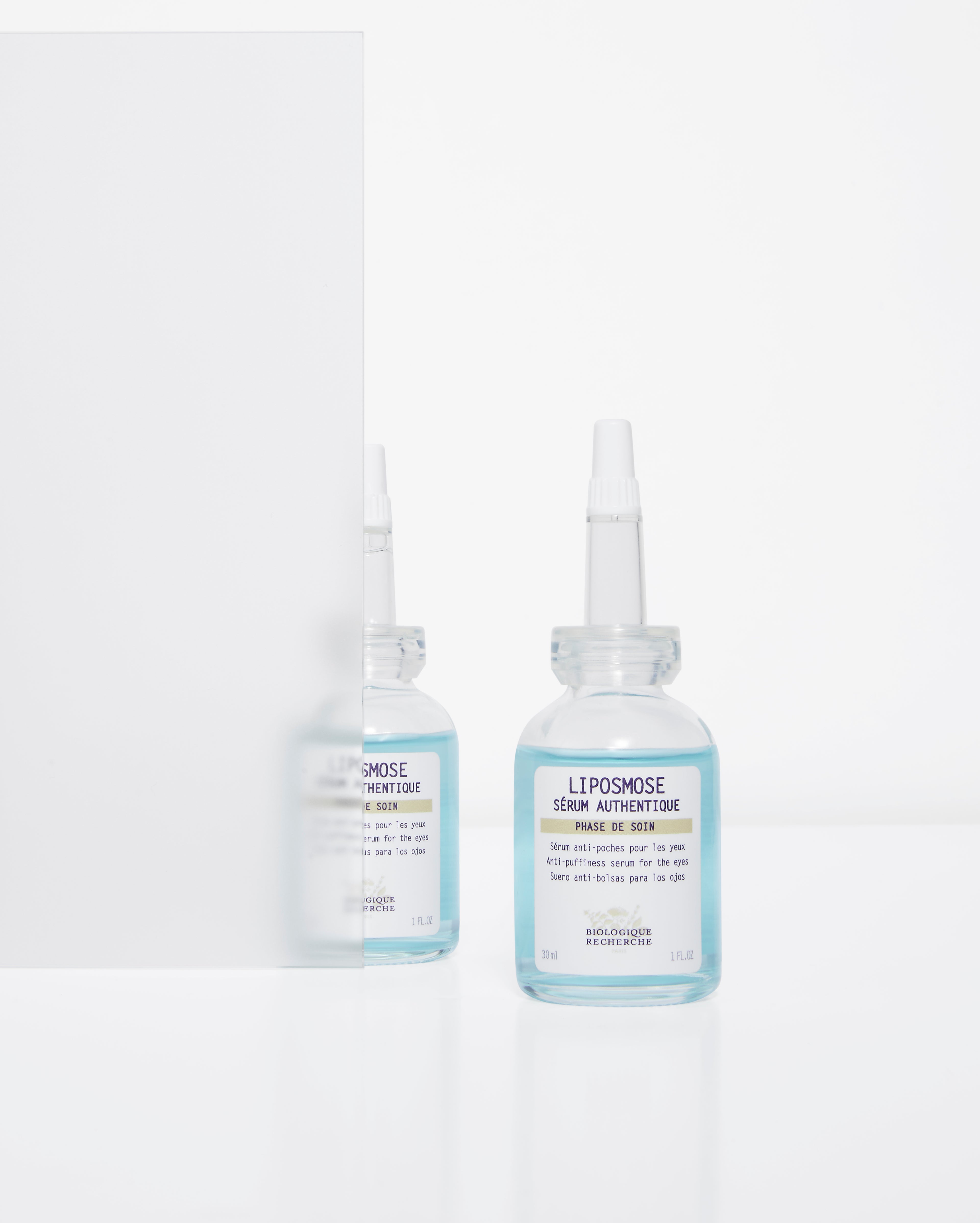 Two clear plastic bottles of Liposmose eye care serum with white caps and blue and white labels against a white background.
