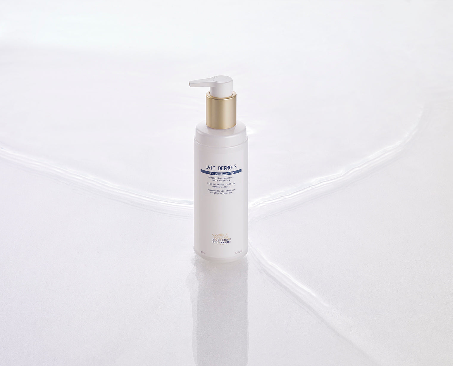 White pump bottle with gold collar labeled Lait Dermo-S on glossy white surface.