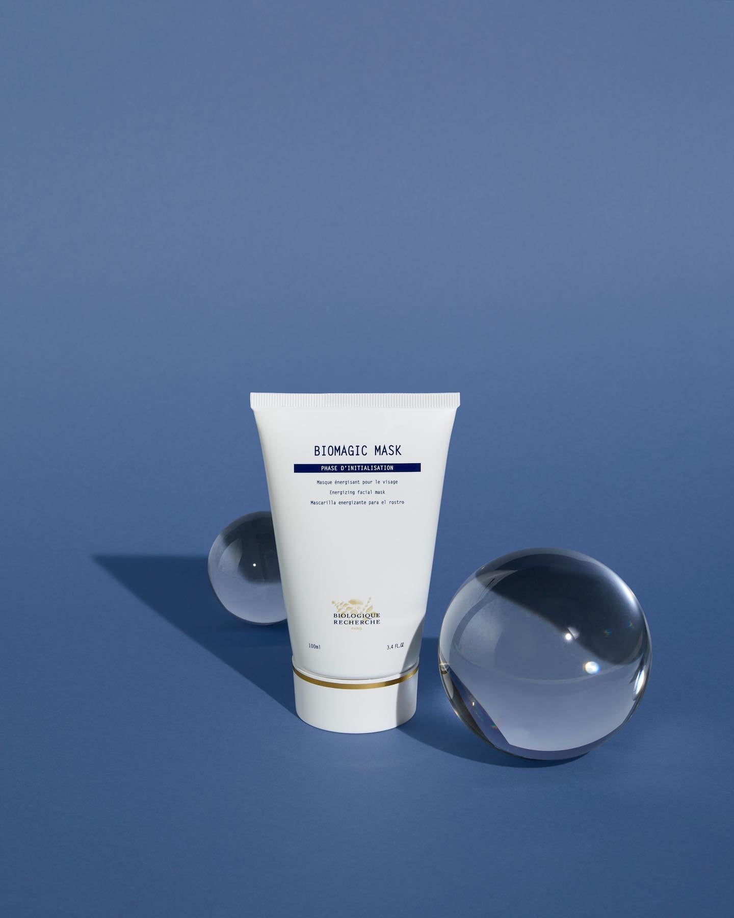 White tube of Biomagic Mask with blue text and gold accents, standing between two clear glass spheres on a blue background.