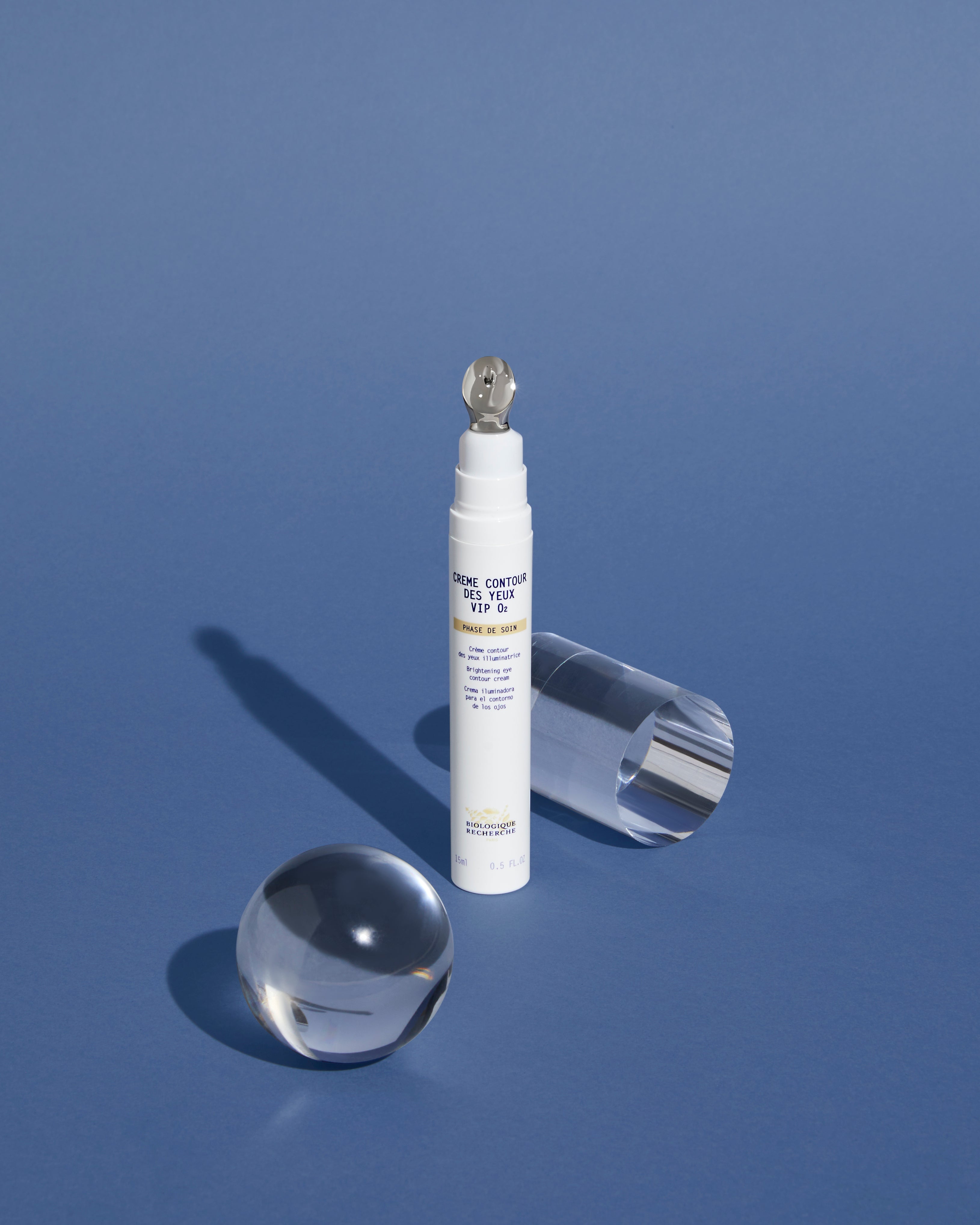 White tube of Crème Contour des Yeux VIP O2 eye cream with metallic roller applicator on blue background.