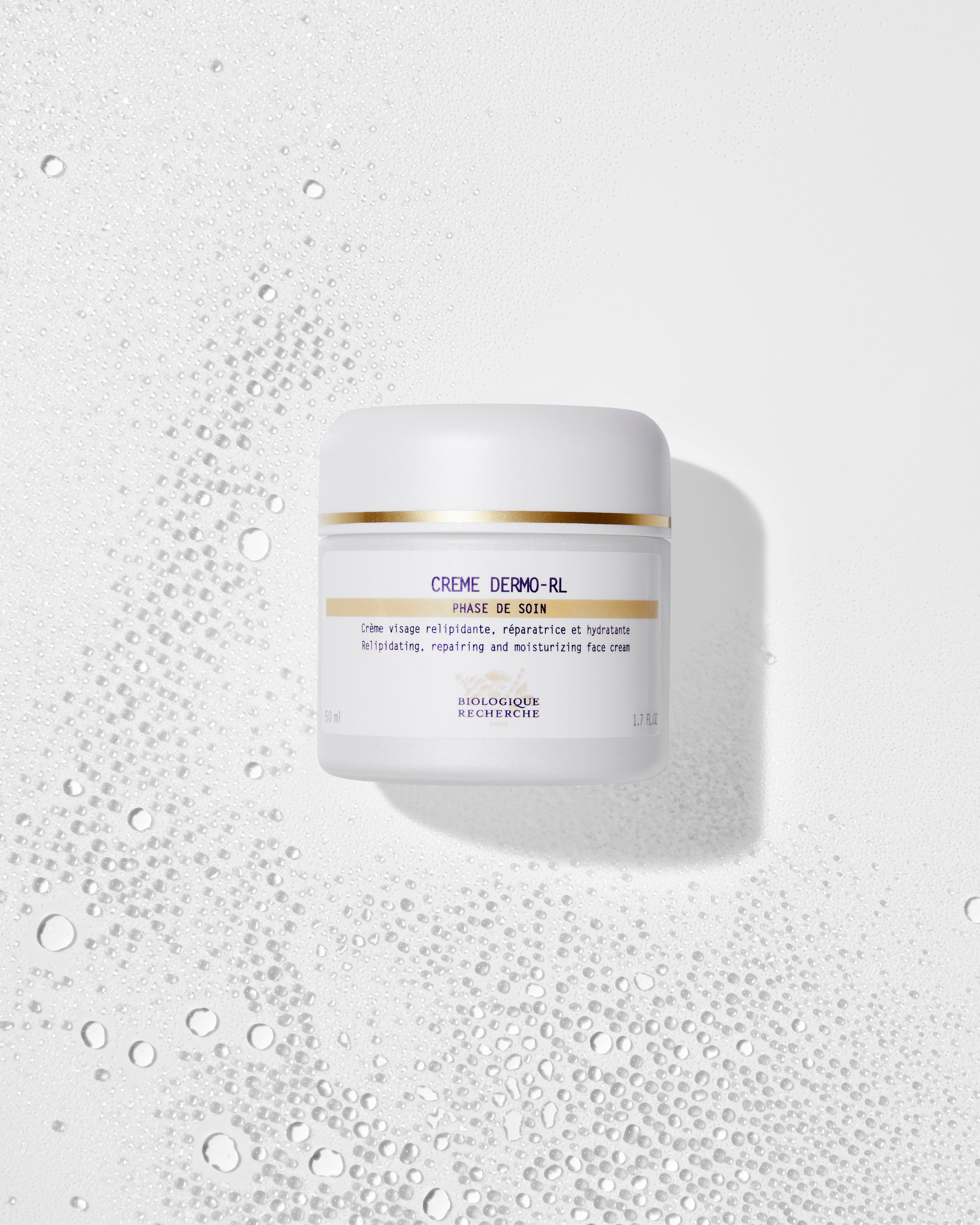 White jar of Crème Dermo-RL moisturizer with gold and blue text on label, surrounded by water droplets on white surface.