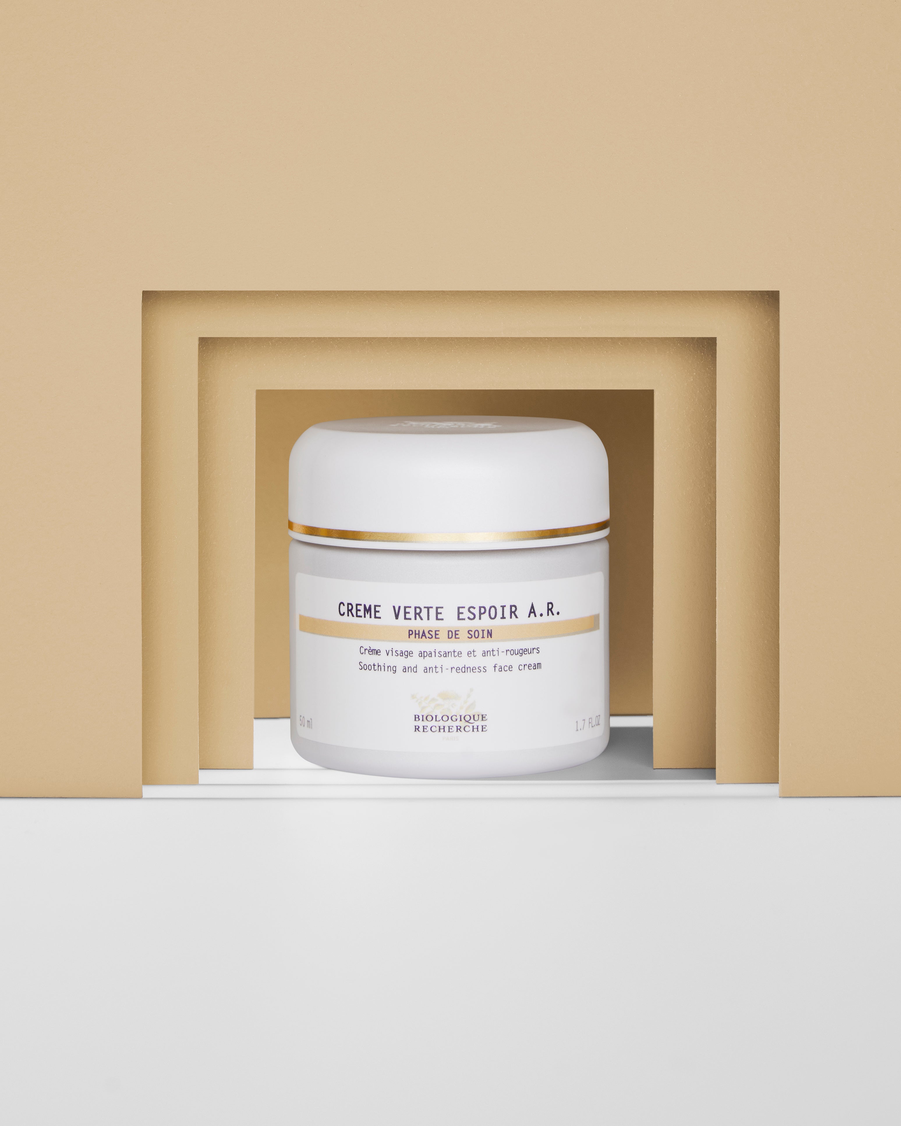 White jar of Crème Verte Espoir A.R. moisturizer with gold and black text on a beige and white geometric background.