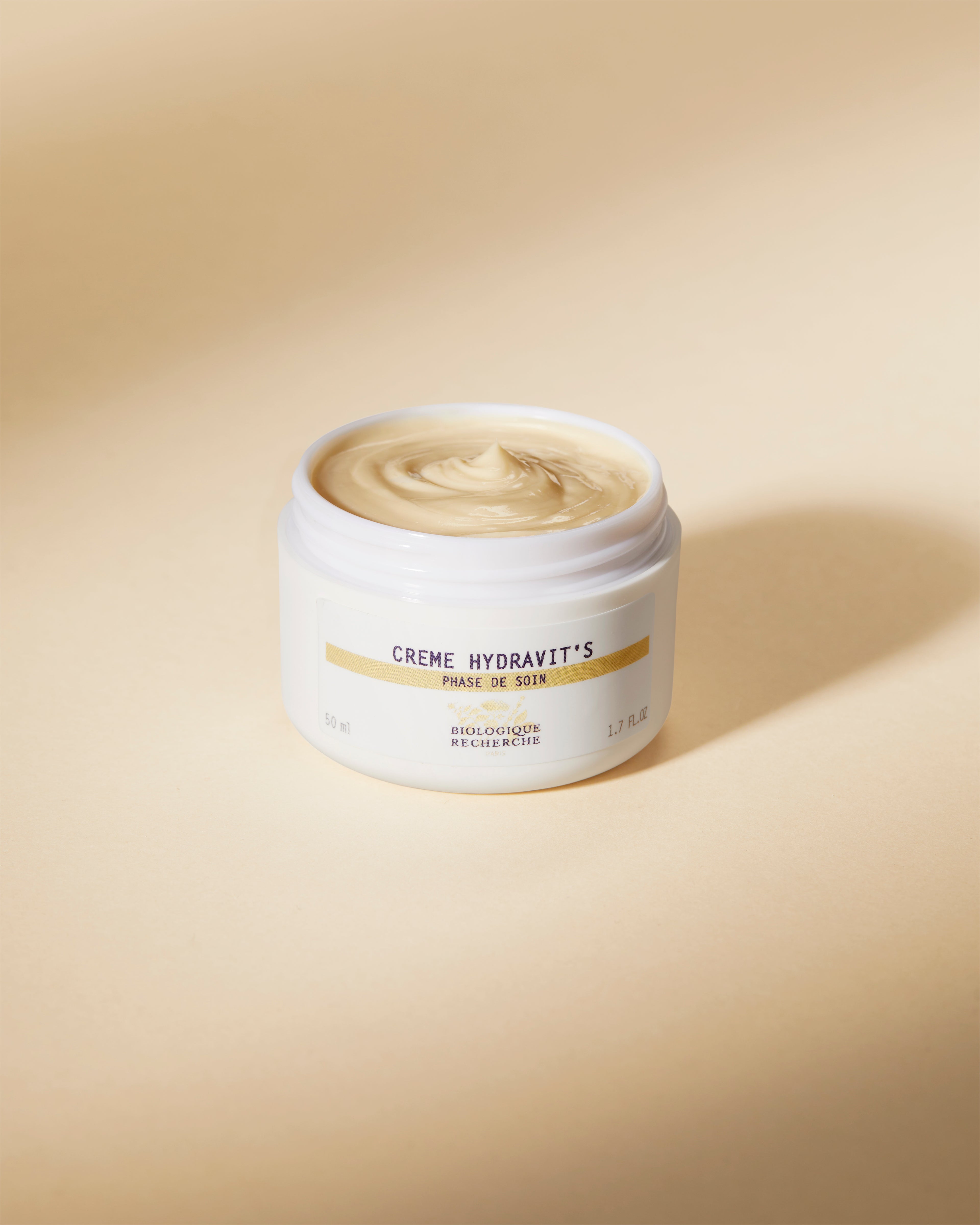 Open jar of beige Crème Hydravit’S moisturizer with smooth creamy texture on light beige background.