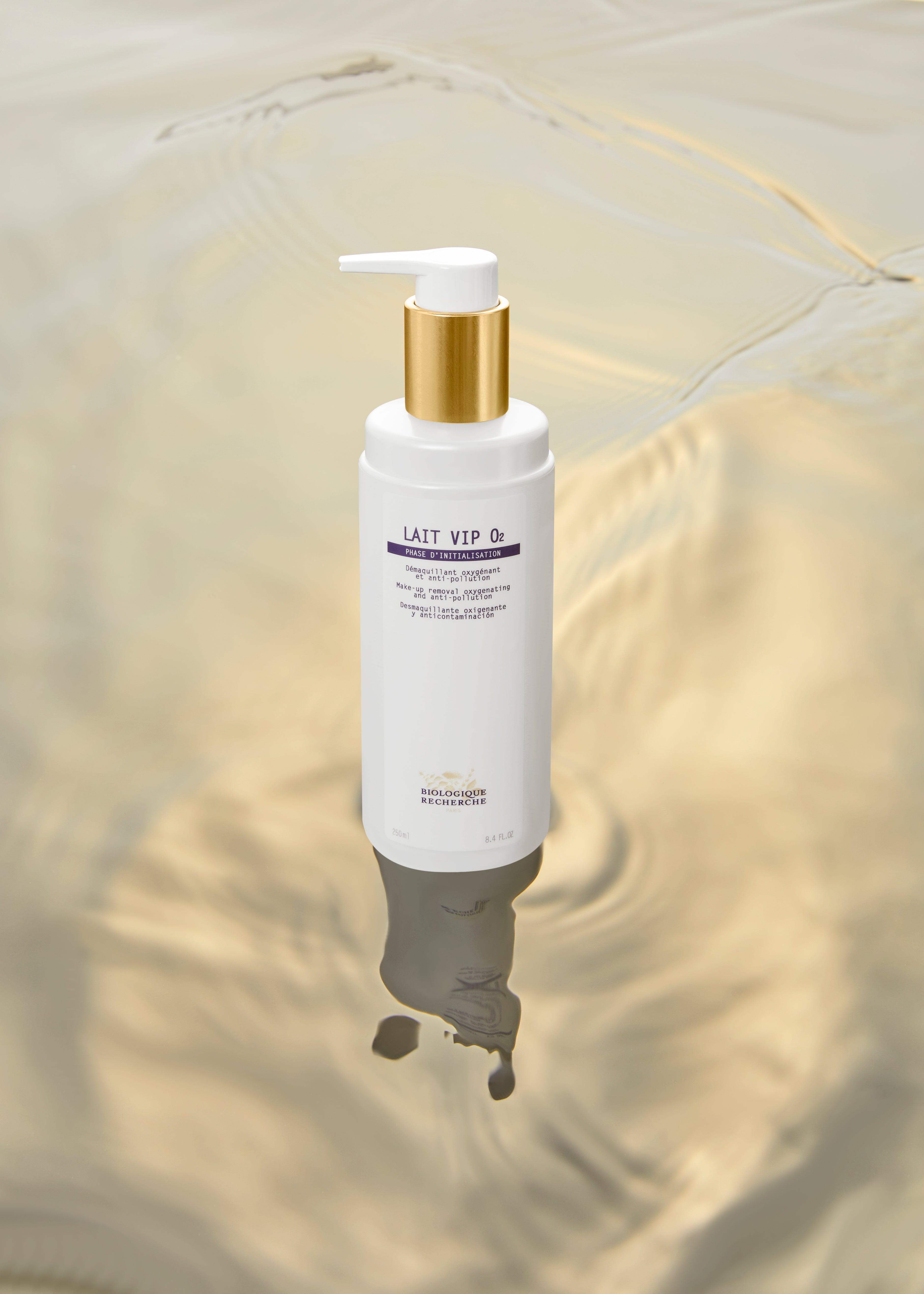 White pump bottle of Lait VIP O2 skincare with gold collar and purple text on wavy beige background.