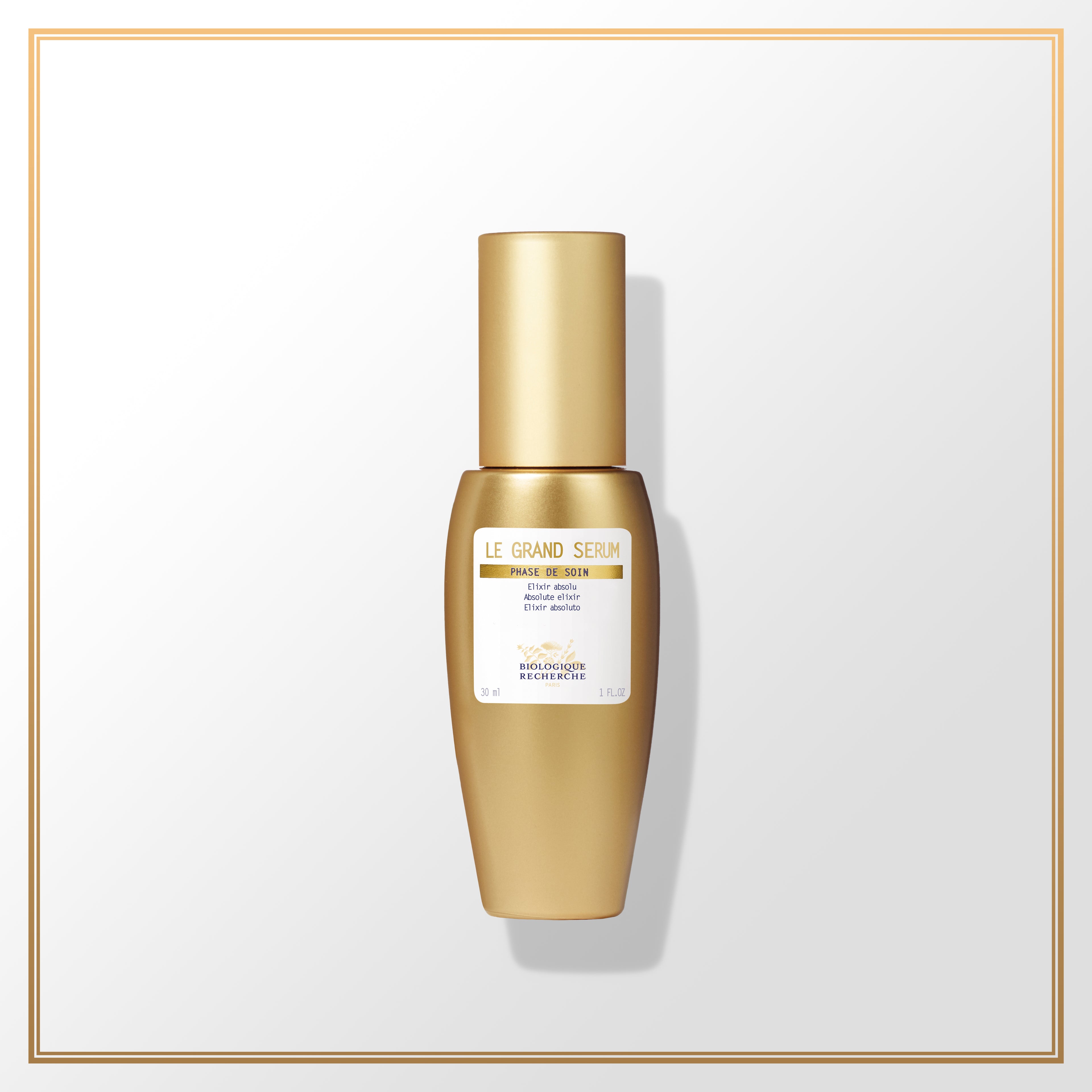 Gold-finished Le Grand Sérum bottle with white label and gold cap on white background.