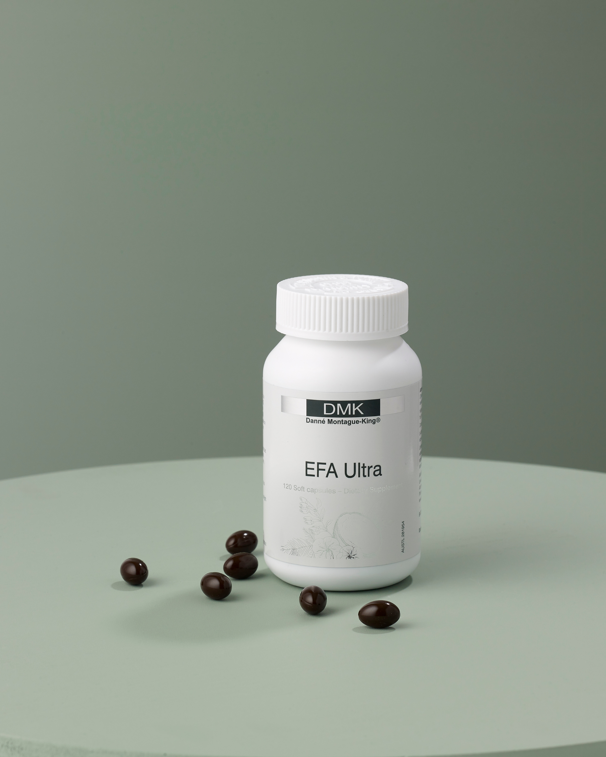 White supplement bottle labeled EFA Ultra with seven dark brown softgel capsules on a green surface.