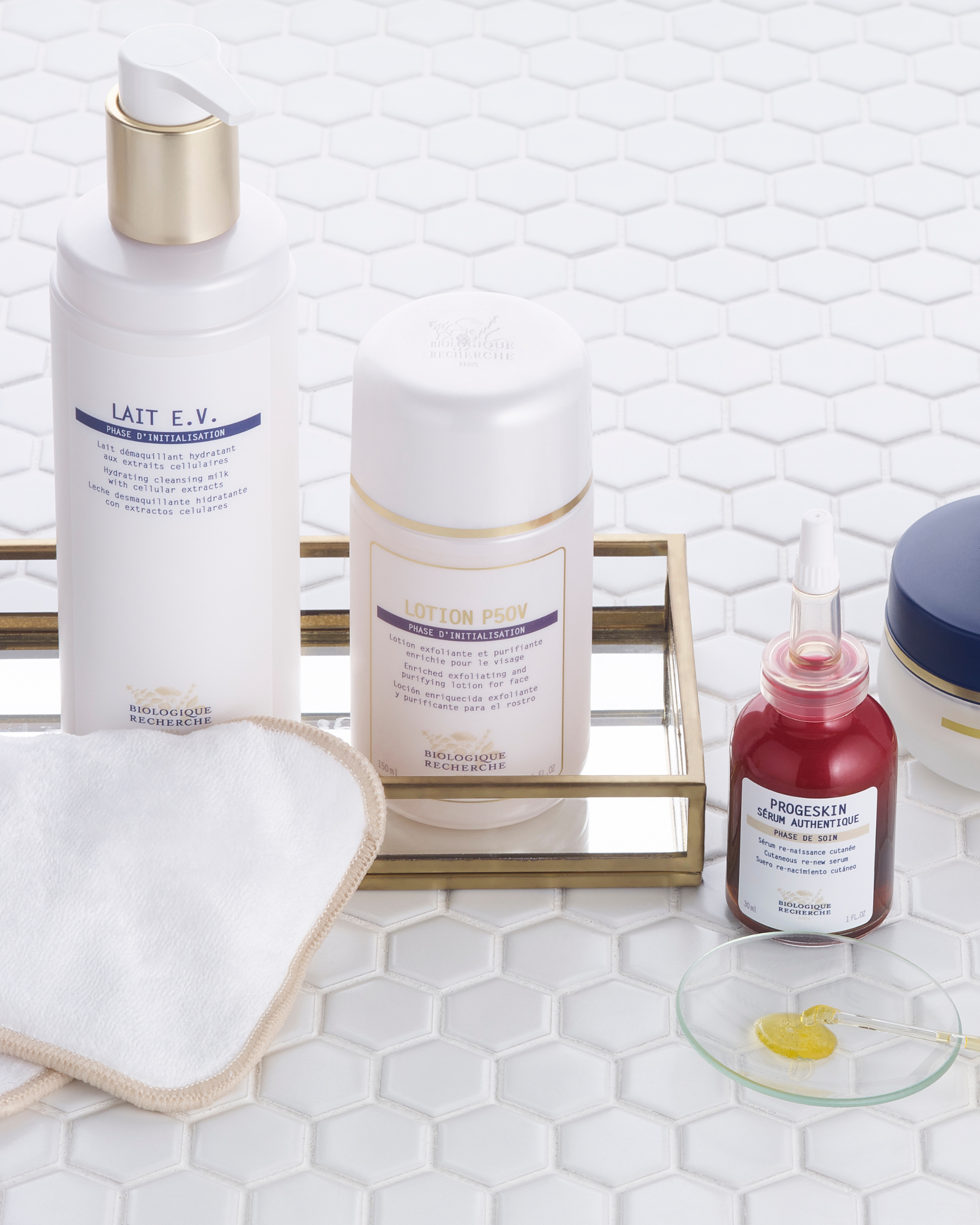 Lait E.V. white bottle with silver pump on hexagonal tile surface with cotton pads and skincare jars.