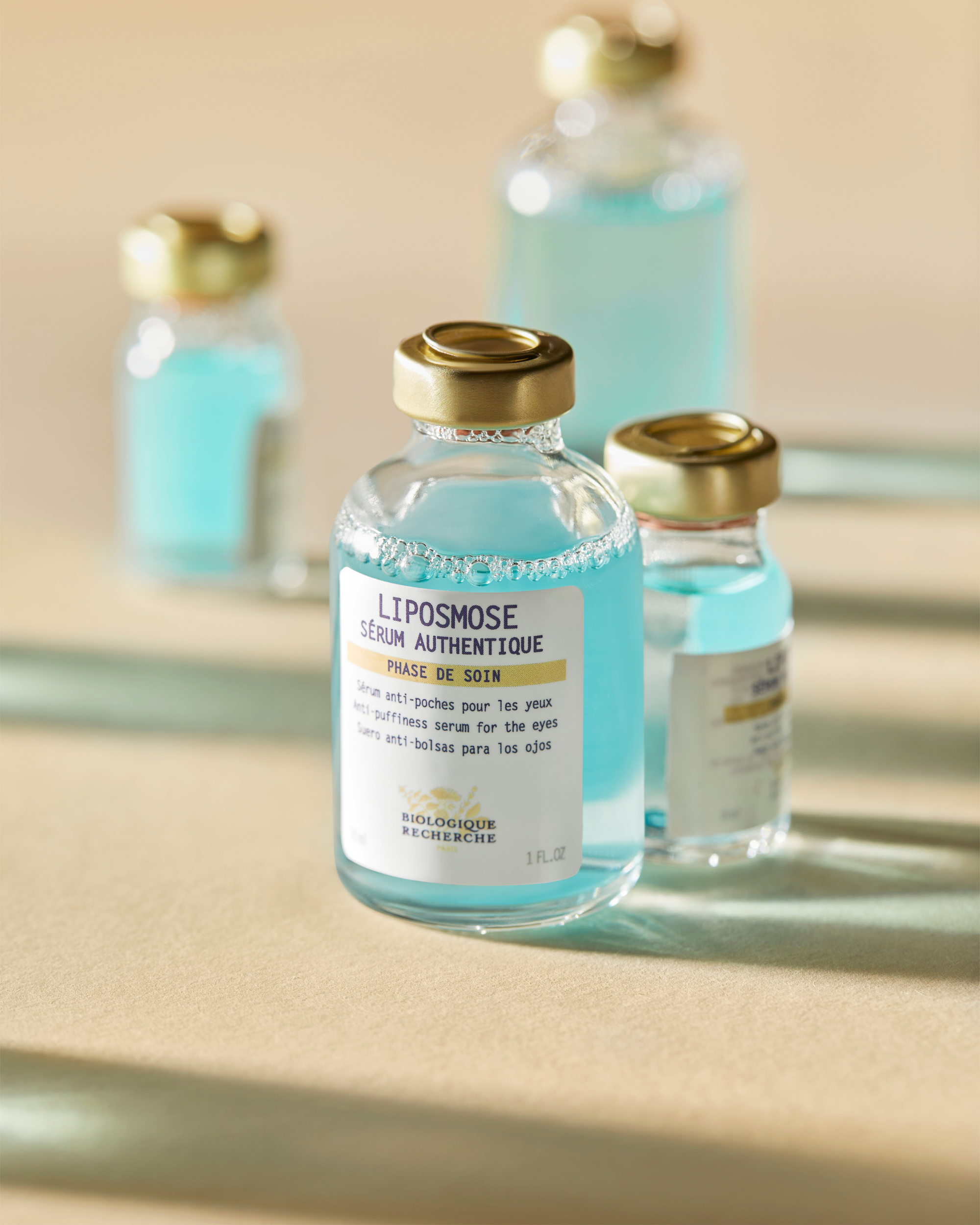 Clear glass bottle of Liposmose eye serum with gold cap and blue liquid inside, labeled in blue and white.